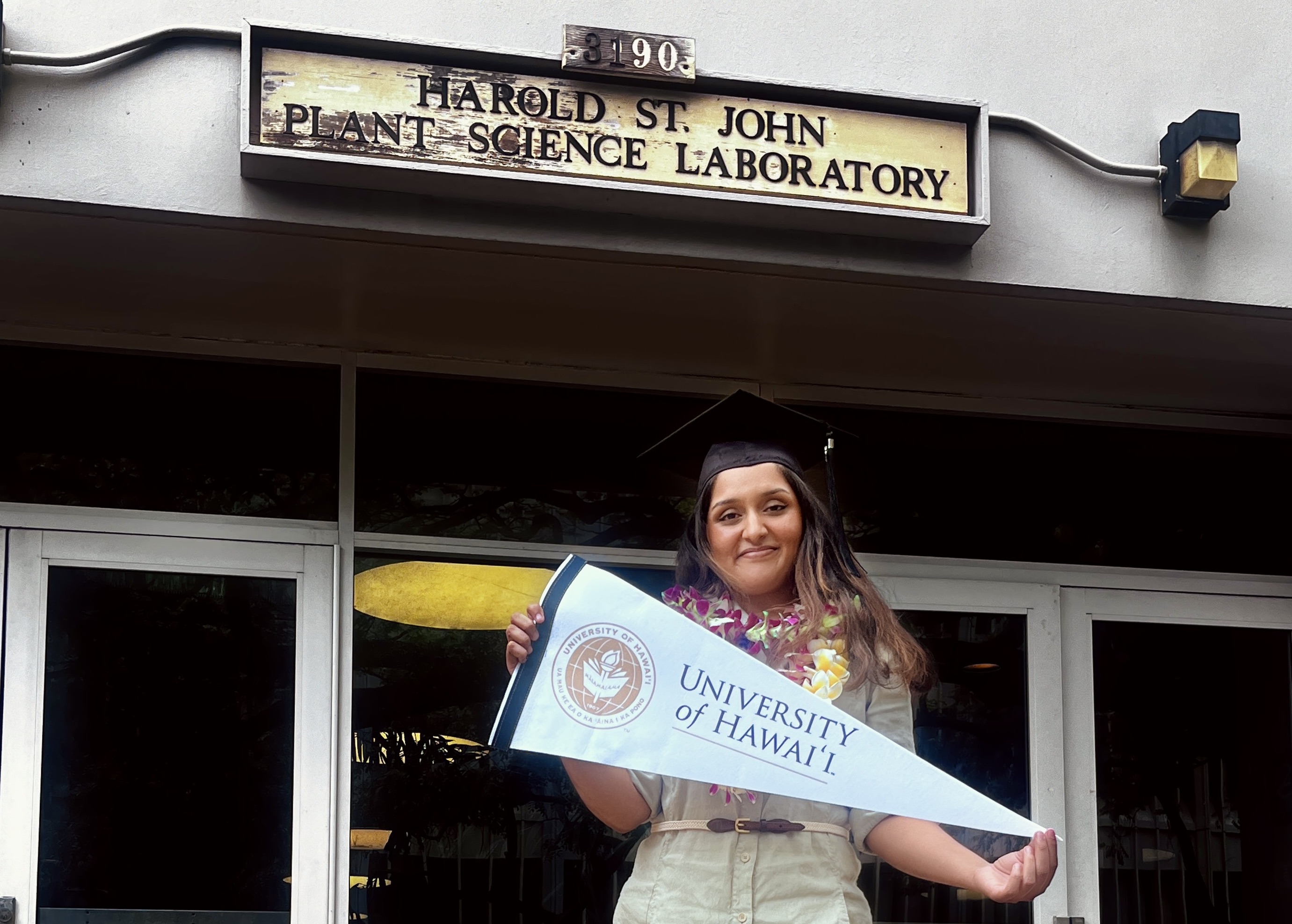 Manya Singh in mortar board holding University of Hawaii banner
